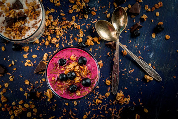 Easy and light healthy dessert of yogurt, fruit smoothies, granola and dark chocolate on a dark blue table, sprinkle dessert ingredients