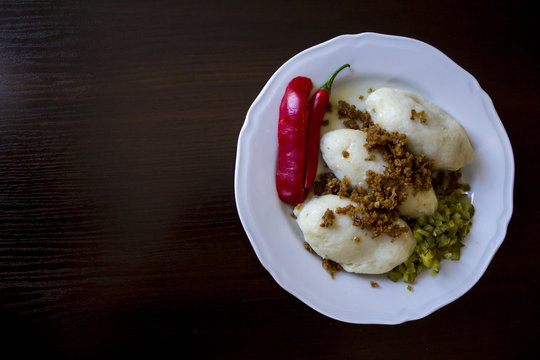 Potato dumplings - a traditional regional dish. Polish and Lithuanian cuisine. With pickles , fried bacon and paprika on a white plate on a dark background .