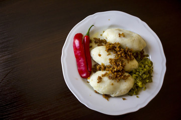 Potato dumplings - a traditional regional dish. Polish and Lithuanian cuisine. With pickles , fried bacon and paprika on a white plate on a dark background .