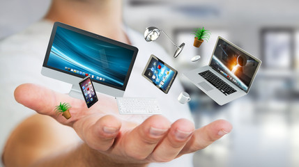Businessman holding flying desk laptop phone and tablet in his h
