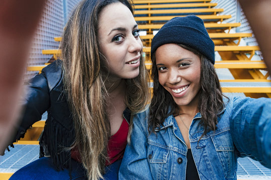 two mixed race female friends sitting and using a smartphone