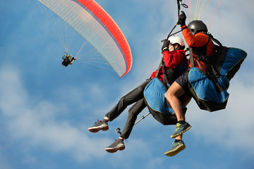 Twee paraglider tandem vliegen tegen de blauwe lucht, tandem paragliden geleid door een piloot
