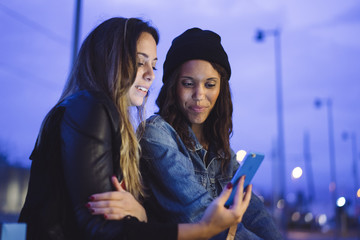 two young female friends chatting and looking at smartphone