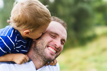 Child playing with his father. Child kissing father. Daddy playing active games with his son outside. Happy family portrait. Laughing dad with little boy enjoying nature together.