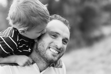 Fototapeta premium Child playing with his father. Daddy playing active games with his son outside. Happy family portrait. Laughing dad with little boy enjoying nature together. Black and white photo.