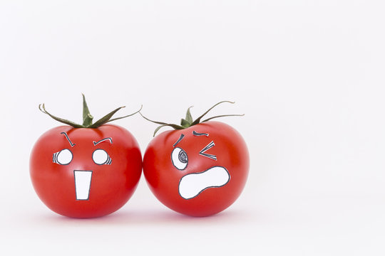 Two fresh red tomatoes with scared faces in front of white background