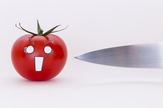 A fresh red tomato with scared face and a sharp knife in front of white background