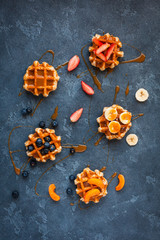 Traditional belgian waffles with fresh fruit and caramel on stone background. Flat lay, top view