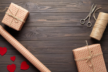 Fototapeta na wymiar Composition with gifts, scissors, wrapping paper, twine, woolen hearts. Packaging of gifts in rustic style on Valentine's Day, a birthday, Mother's Day or Christmas. Dark wooden background.