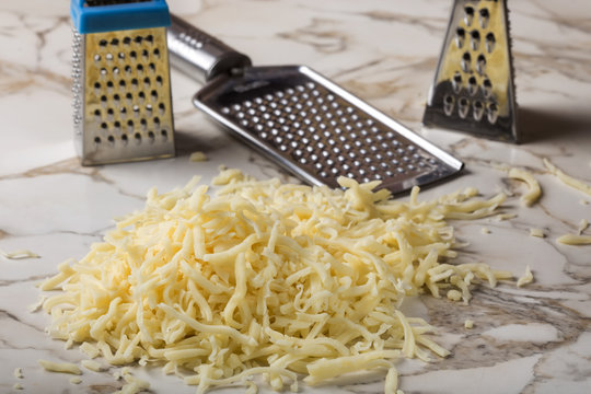 Grated mix cheese and three stainless steal graters in backgroun