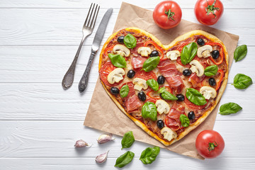 Heart pizza love concept Valentine's Day romantic dinner Italian homemade baked food. Prosciutto, olives, champignon mushrooms, basil and mozzarella meal served on white wooden table
