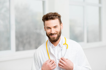 Portrait of a handsome smiling doctor in uniform in front of the window in the white hospital interior