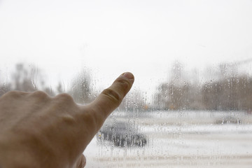 Index finger of hand concerns blurred glass of rain