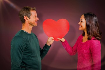 Composite image of smiling couple holding red heart shape 