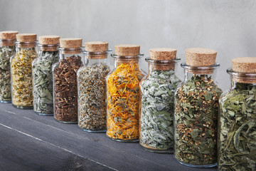 Different kinds of herbs for tea inside glass bottles. - obrazy, fototapety, plakaty