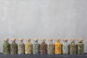 Different kinds of herbs for tea inside glass bottles.