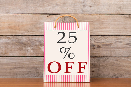 Shopping bags with inscription "25% OFF" on wooden background - Powered by Adobe