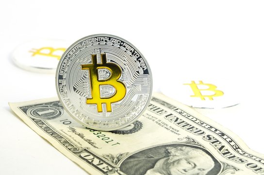 Bitcoin coin laying on paper dollar bill