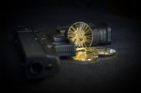 Shiny gold Bitcoin coin with gun on black background