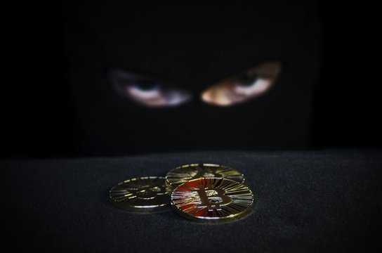 Shiny gold bitcoin coin and masked man face on background