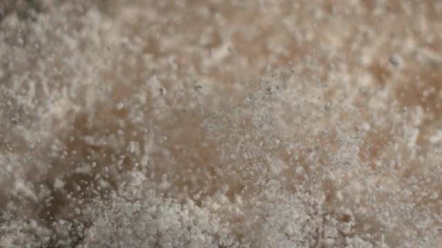 White powder particles bounce off canvas from an impact and fall in slow motion