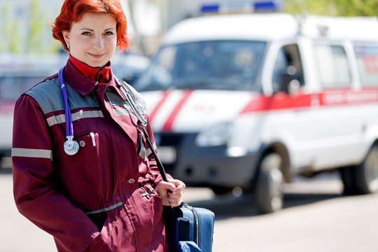 Positive female paramedic with ambulance bag on ambulance car background