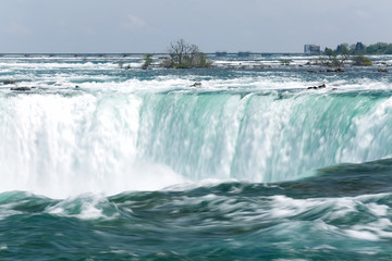 The bright blue water of Niagara Falls flows down the river and over the waterfall in spring