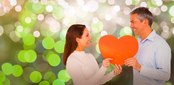 Composite image of smiling couple holding heart shape paper