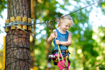 Adorable little girl enjoying her time in climbing adventure park on warm and sunny summer day