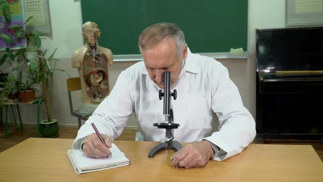 A college professor working with microscope and taking notes in the classroom