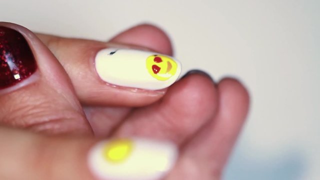 Manicure procedure female hand drawing yellow emoji on white finger nail polish, close up