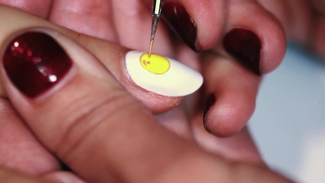 Manicure procedure woman hand painting yellow emoji on white finger nail polish, close up