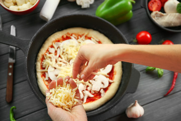 Woman making pizza in pan on wooden table