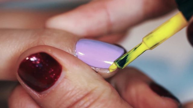 Manicure procedure woman hand drawing yellow stripe on purple finger nail polish, close up