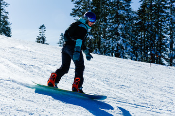Young caucasian woman wearing black jacket and helmet snowboards on a clear blue day