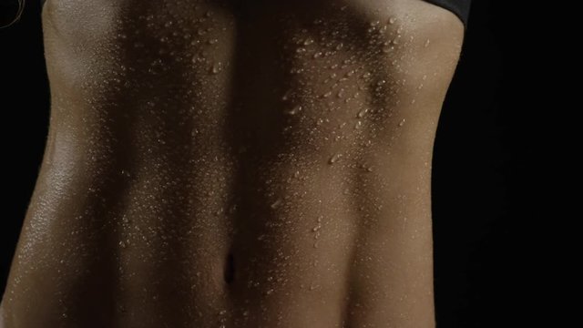 Sweep across woman's abs, glistening with sweat as she works out. Over black.