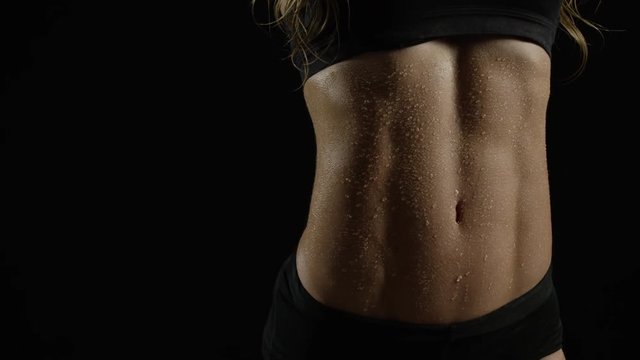 Sweep across woman's toned abs, glistening with sweat. Over black BG.