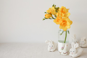 Easter bunny rabbits and yellow Freesia flowers in vase on white linen table