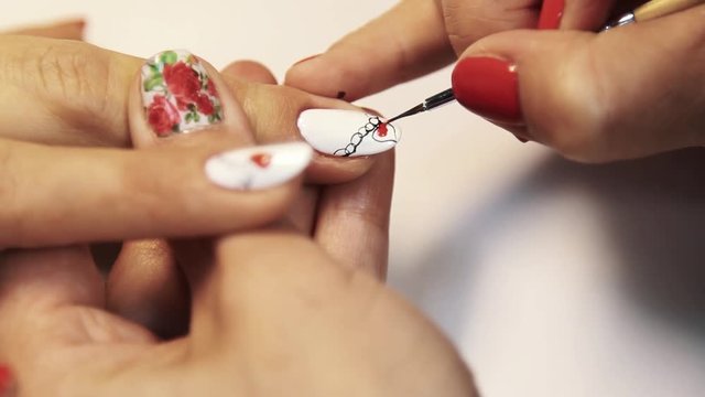 Cosmetic shop manicure session, woman hand painting heart picture on white nail polish, close up