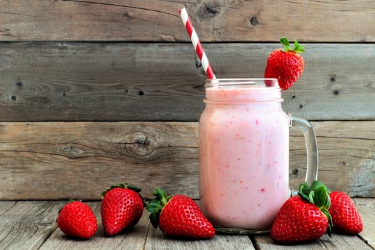 Healthy strawberry smoothie in a mason a jar glass with scattered berries over a rustic wood background