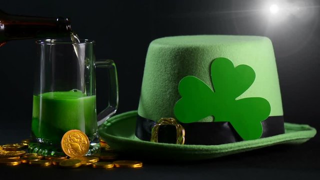 St Patricks Day pouring green beer with green leprechaun hat, gold coins and shamrock against black background, static with lens flare.