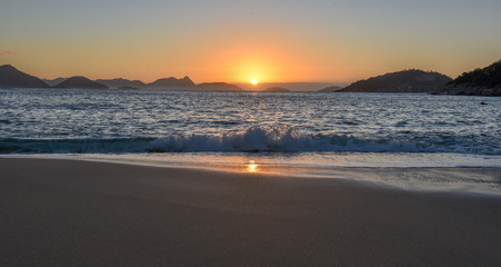Obraz premium Beautiful Sunrise with the sun rising out of the ocean at the Red Beach, Praia Vermelha, with the Sugarloaf Mountain, Rio de Janeiro
