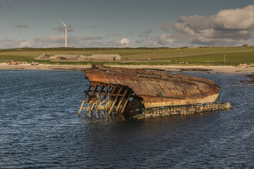 Orkneys, Scotland - June 5, 2012: Closeup of remains of a WW II warship wreck near Weddell Bay. Brown rusty carcass fronted by lobster trap contraption. Small green band of land splits image in two