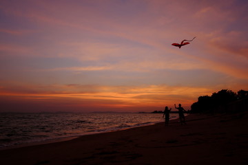 Boy and girl playing a kite on the beach. Twilight sky background.