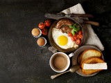 breakfast in a frying pan, fried eggs, sausages and tomatoes on a dark background