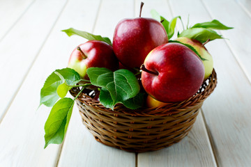 Ripe apples with leaves in the basket on wooden table