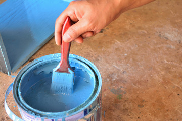 hand with paint brush, dip into the paint bucket