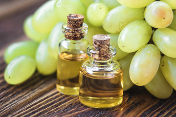 Healing grapes seeds oil in a glass jar, fresh grapes on old wooden background, seed extract has antioxidant and nourishing the skin, spa concept, selective focus macro front view. Bio, eco products.