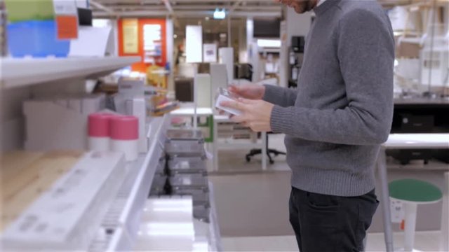 portrait of young cheerful man choosing acrylic paint color in tube in art shop