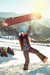Girl snowboarder standing on a mountain top keeps, snowboard over the head